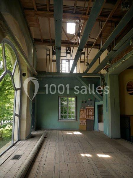 Intérieur d'une pièce lumineuse avec poutres apparentes, grandes fenêtres et parquet en bois clair.