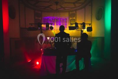 Serre illuminée au crépuscule, entourée de murs en pierre et d'arbres, avec une tour en arrière-plan.