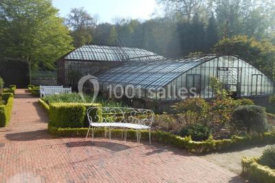 Serre illuminée au crépuscule, entourée de murs en pierre et d'arbres, avec une tour en arrière-plan.