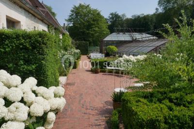 Serre illuminée au crépuscule, entourée de murs en pierre et d'arbres, avec une tour en arrière-plan.