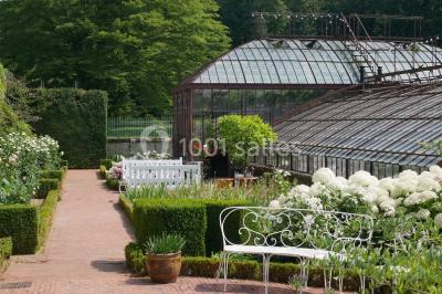Serre illuminée au crépuscule, entourée de murs en pierre et d'arbres, avec une tour en arrière-plan.