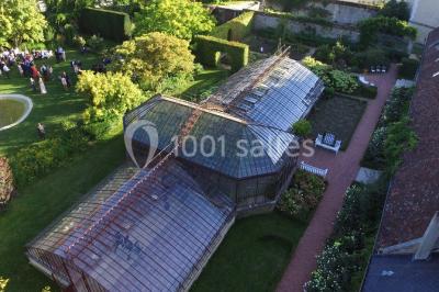 Serre illuminée au crépuscule, entourée de murs en pierre et d'arbres, avec une tour en arrière-plan.