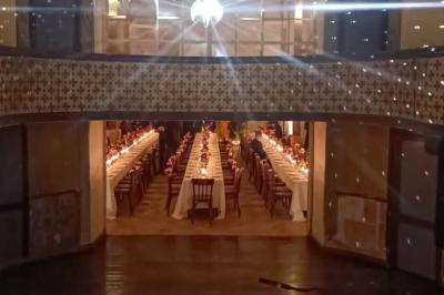 Serre illuminée au crépuscule, entourée de murs en pierre et d'arbres, avec une tour en arrière-plan.