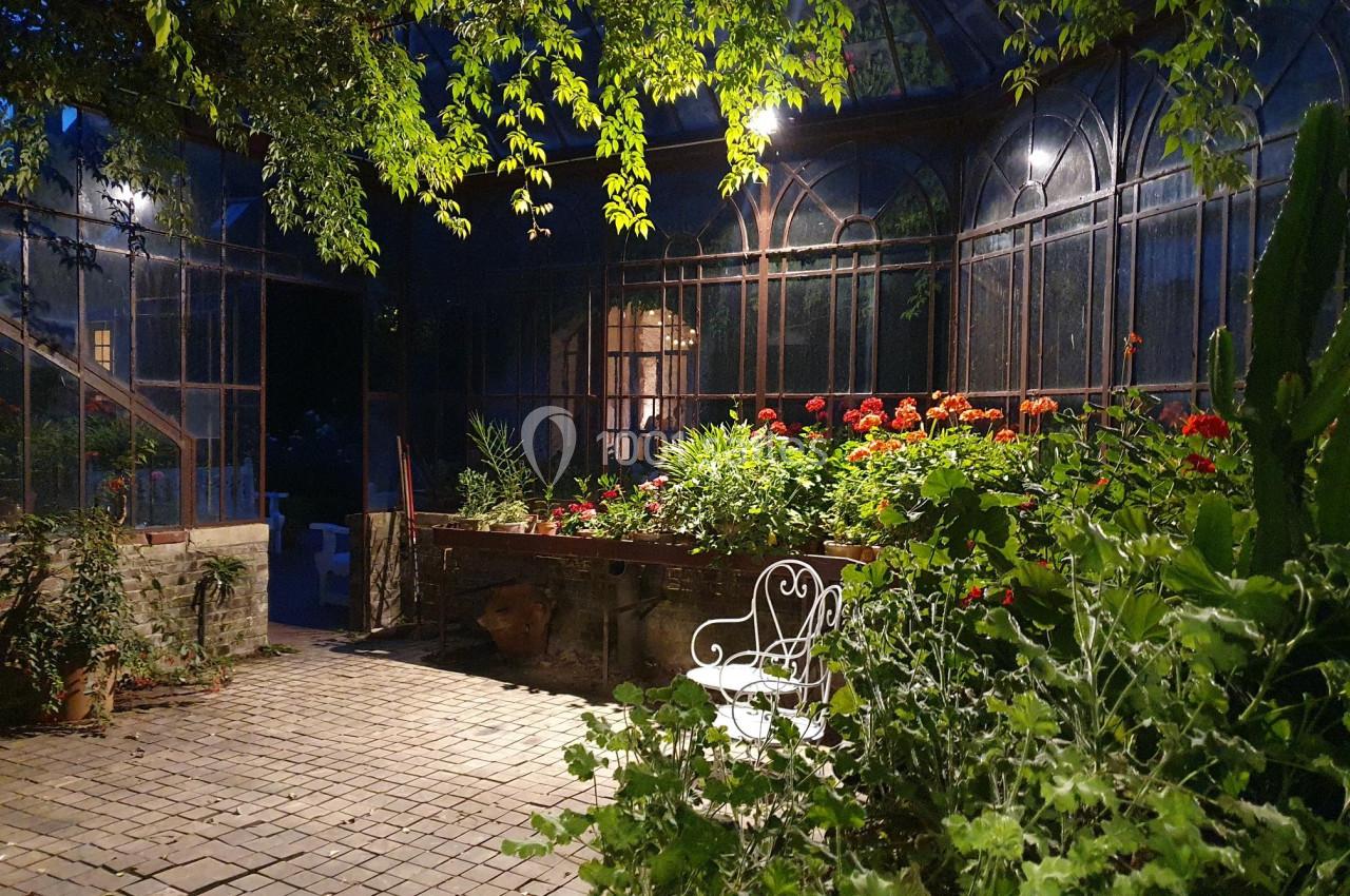 Serre lumineuse en soirée avec des plantes verdoyantes, fleurs colorées et une chaise blanche en fer forgé.