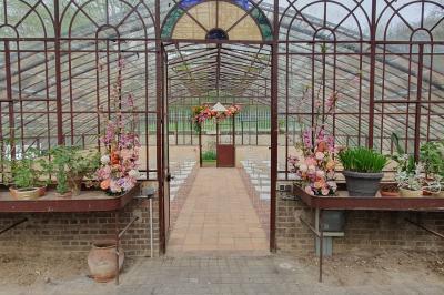 Serre illuminée au crépuscule, entourée de murs en pierre et d'arbres, avec une tour en arrière-plan.