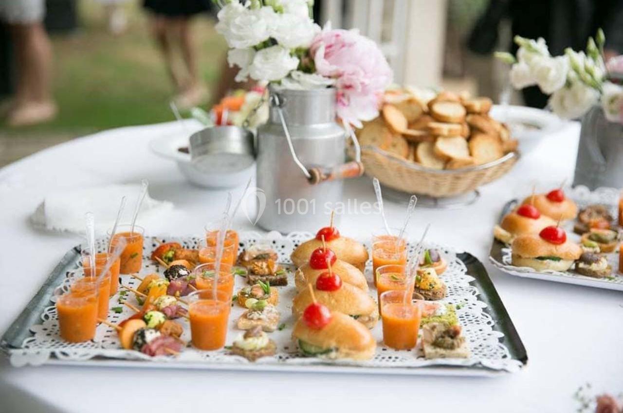Plateaux de bouchées apéritives variées avec verrines et petits pains, disposés sur une table décorée de fleurs.