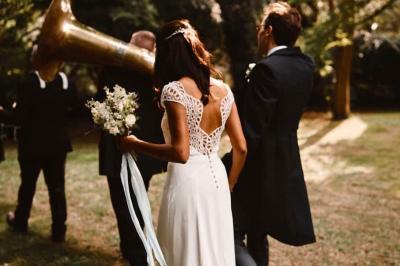 Bâtisse en pierre avec toit en tuiles, entourée de végétation et d'un chemin sous un ciel bleu clair.