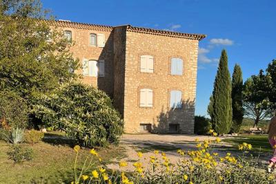 Bâtisse en pierre avec toit en tuiles, entourée de végétation et d'un chemin sous un ciel bleu clair.