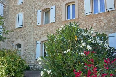 Bâtisse en pierre avec toit en tuiles, entourée de végétation et d'un chemin sous un ciel bleu clair.