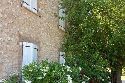 Bâtisse en pierre avec toit en tuiles, entourée de végétation et d'un chemin sous un ciel bleu clair.