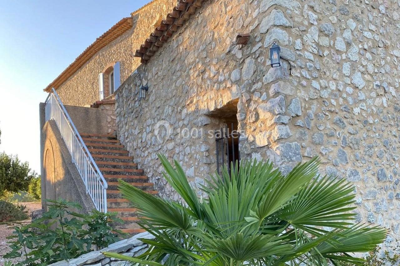 Façade en pierre d'une maison traditionnelle avec escalier extérieur et végétation au premier plan.