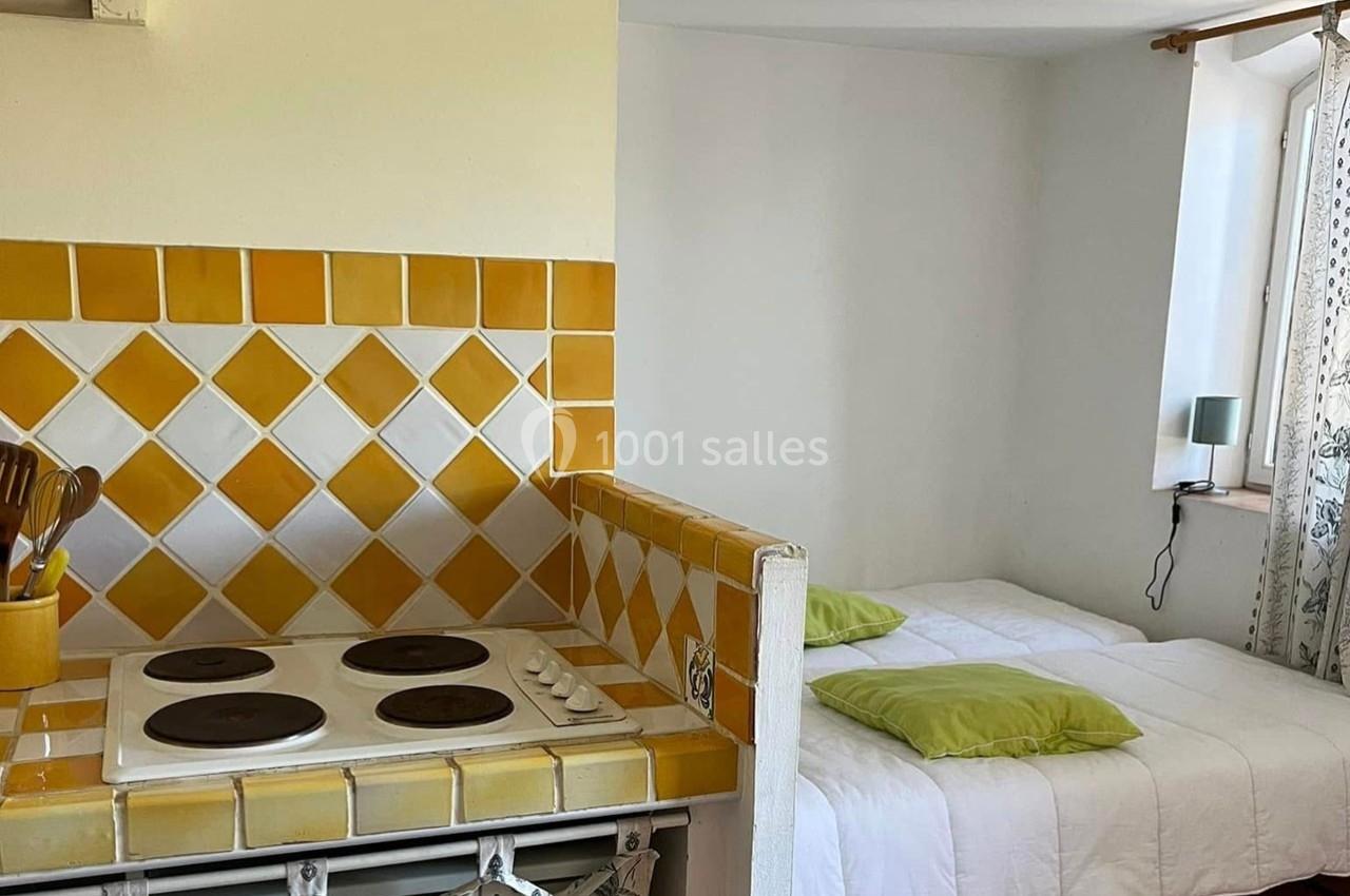 Cuisine avec plaques de cuisson et crédence en carreaux jaunes, attenante à une chambre avec lit et coussins verts.