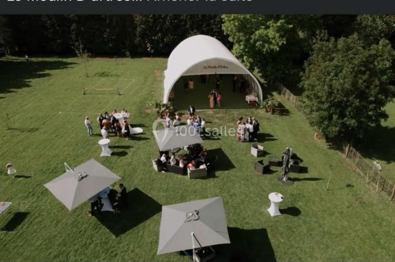 Vue aérienne d'un événement en plein air avec des invités, des tentes, des tables et un chapiteau blanc sur une pelouse.