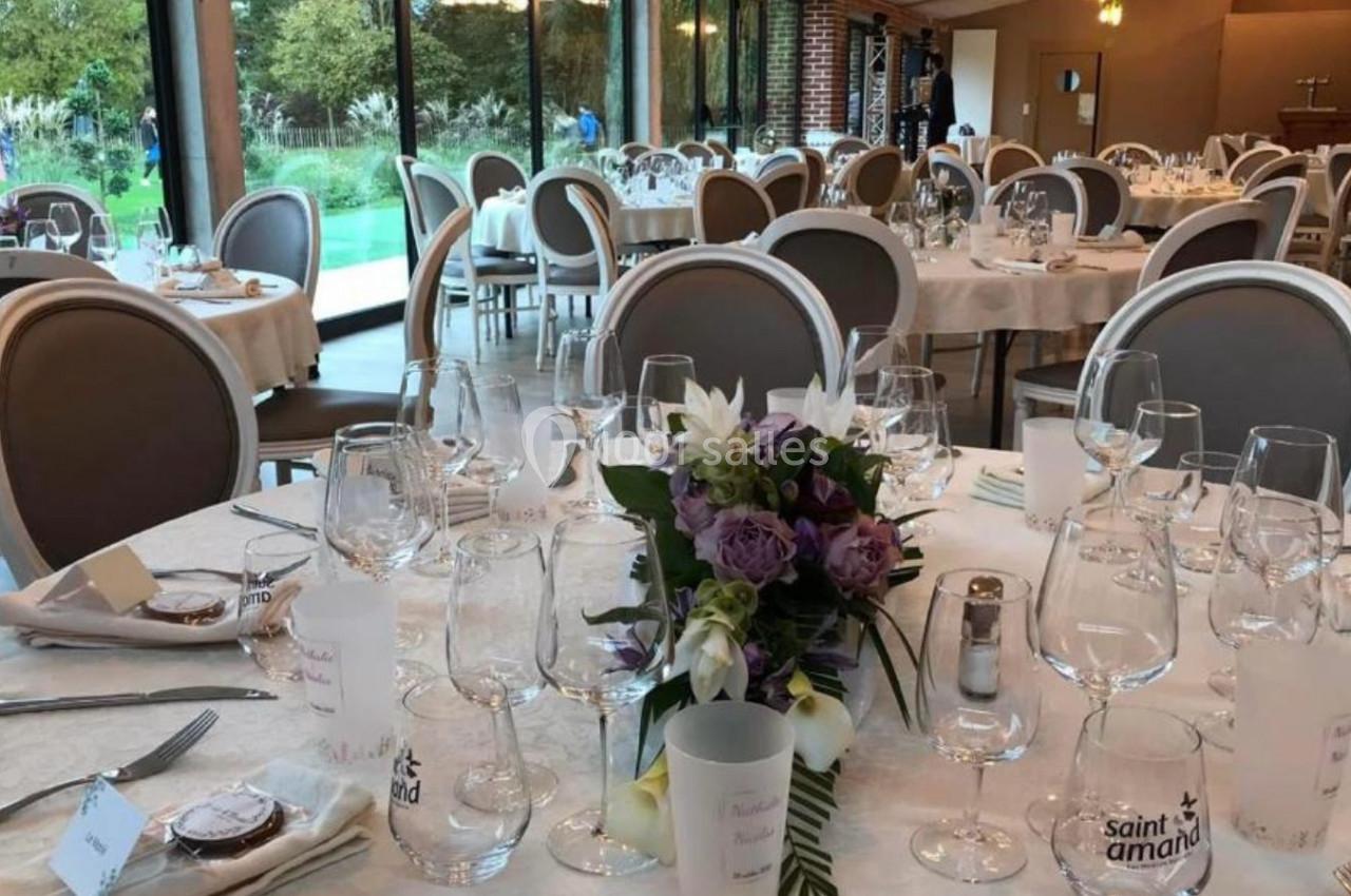 Salle de réception élégante avec tables dressées, décor floral et grandes baies vitrées donnant sur un jardin.