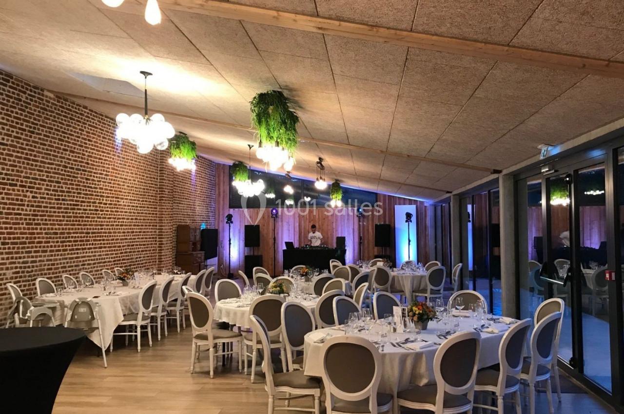 Salle de réception décorée avec des tables dressées, des chaises blanches et des suspensions végétales.