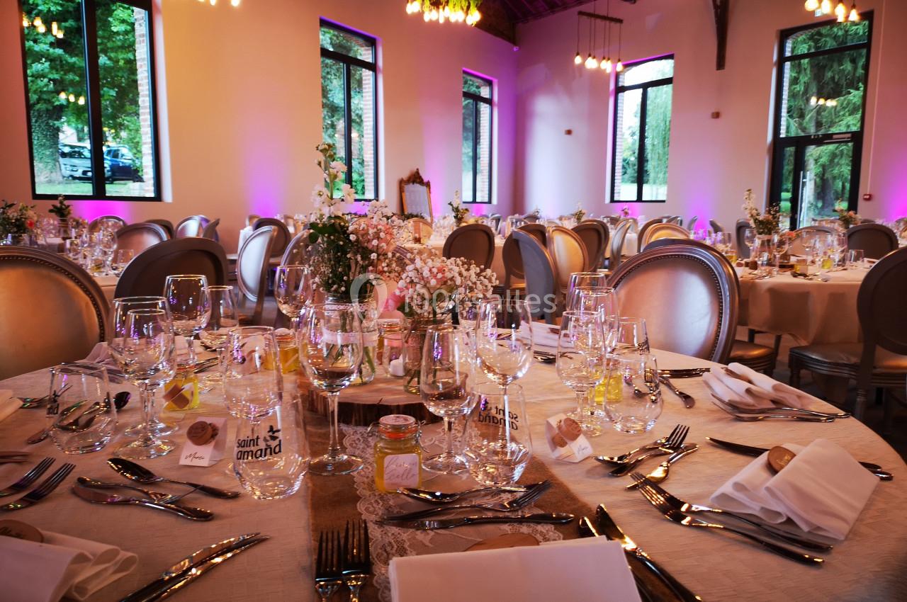 Salle de réception décorée avec des tables rondes élégamment dressées, éclairée par des lumières chaudes et des fenêtres…