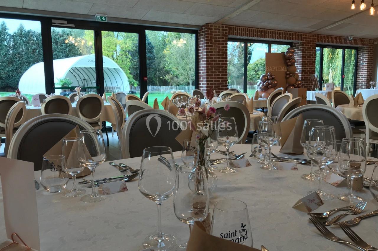 Salle de réception décorée avec des tables dressées, vue sur un jardin à travers de grandes baies vitrées.