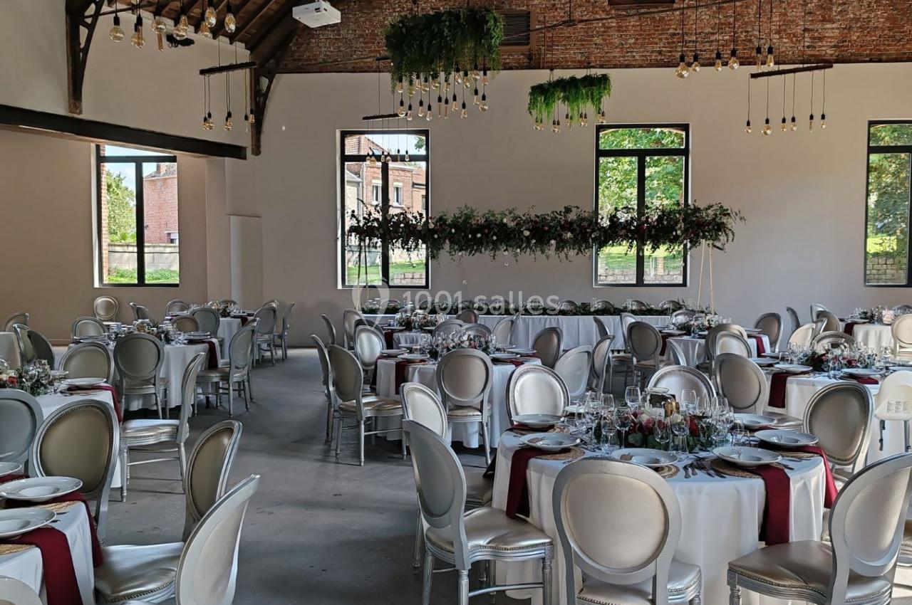 Salle de réception lumineuse avec tables rondes décorées de nappes blanches, chemins de table rouges et compositions…