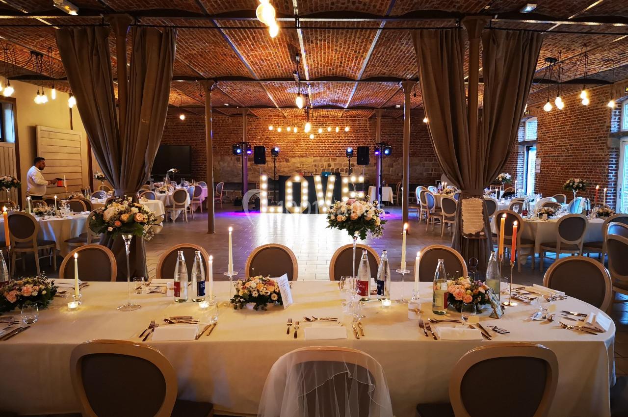 Salle de réception décorée pour un mariage, avec tables dressées, chandeliers et lettres lumineuses ’LOVE’.