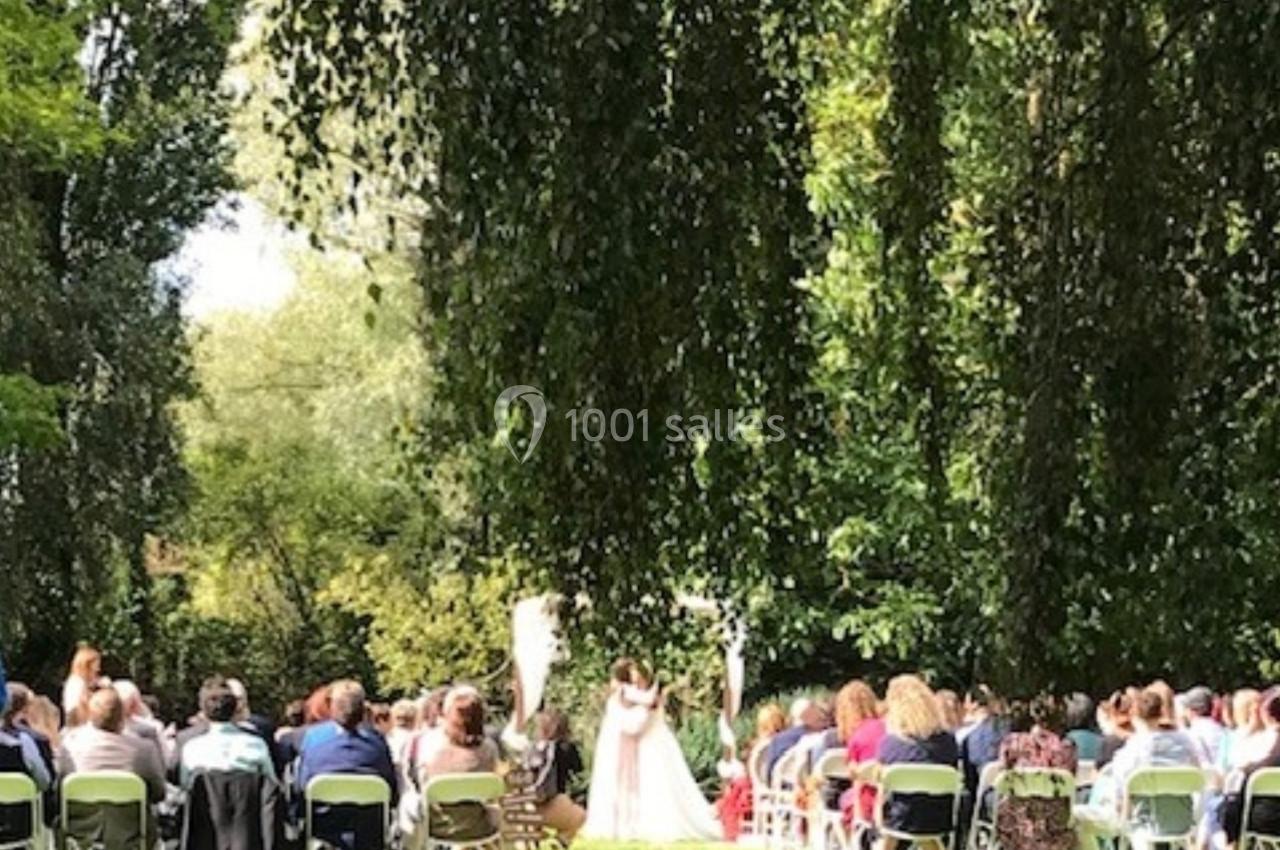 Cérémonie de mariage en plein air avec des invités assis sur des chaises, entourés de verdure et d'arbres.