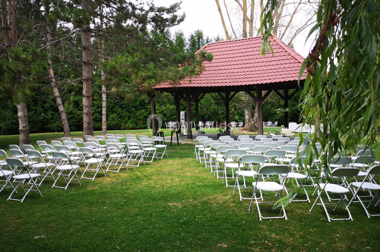 Chaises blanches disposées en rangées devant une pergola en bois rouge, dans un jardin verdoyant.