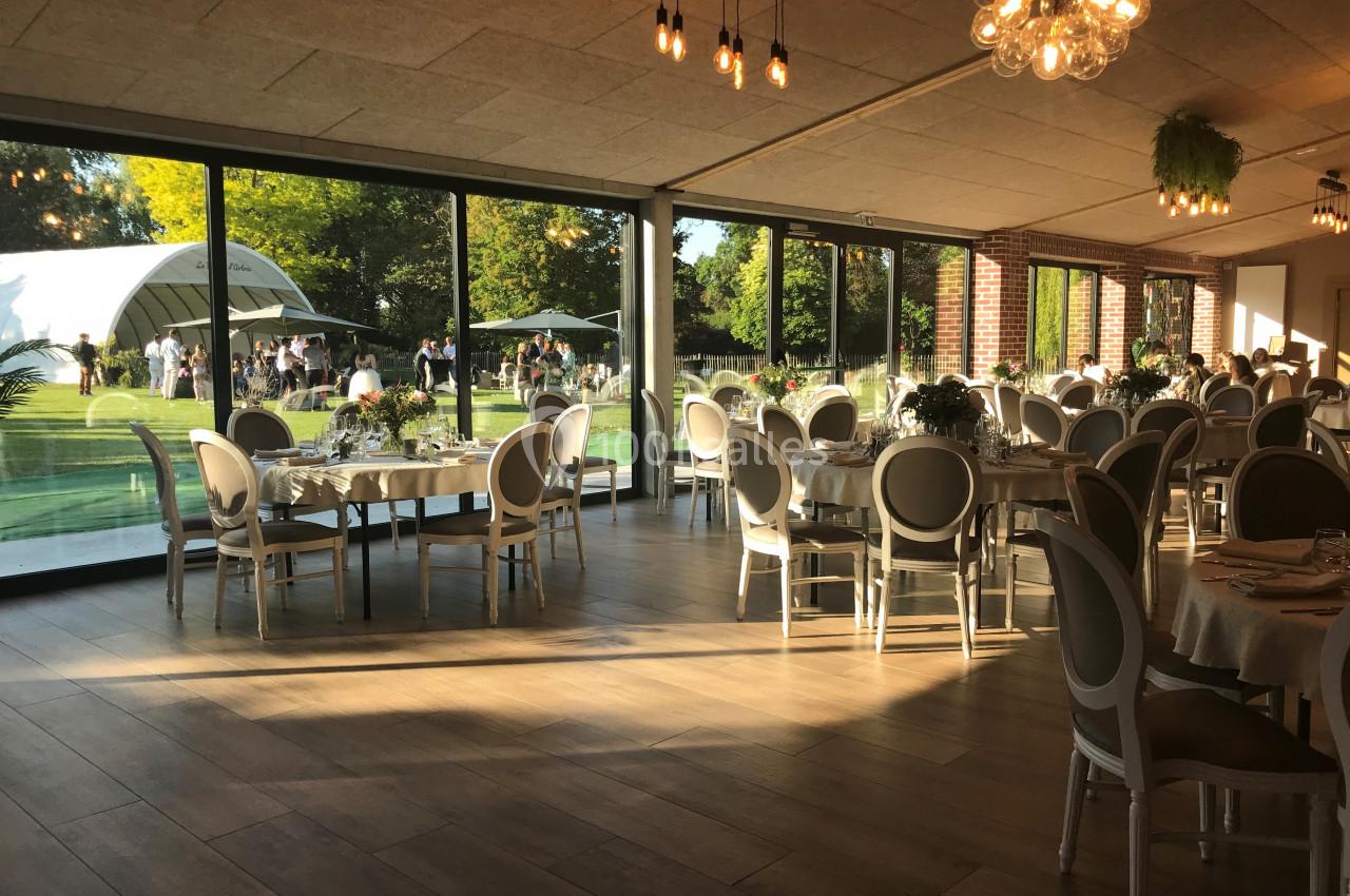 Salle de réception lumineuse avec des tables dressées, donnant sur un jardin et des invités à l'extérieur.