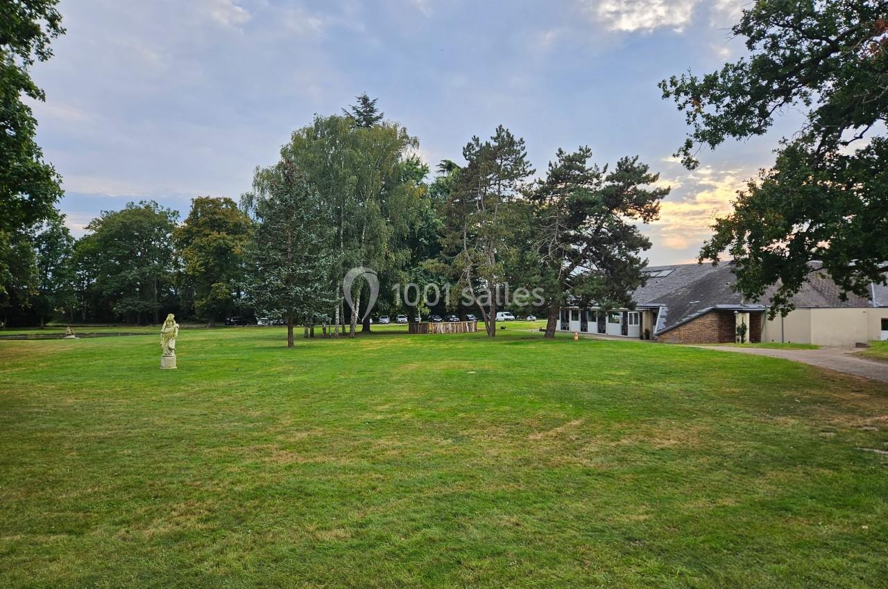 Pelouse verdoyante avec quelques arbres, une statue sur la gauche et un bâtiment à toit en ardoise à droite.