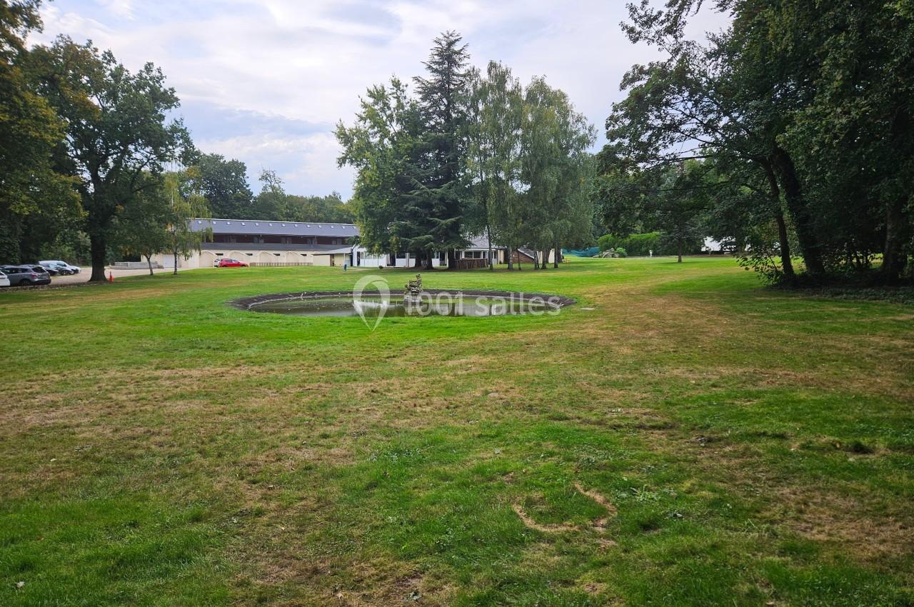 Pelouse avec un petit bassin circulaire au centre, entourée d'arbres et de bâtiments en arrière-plan.