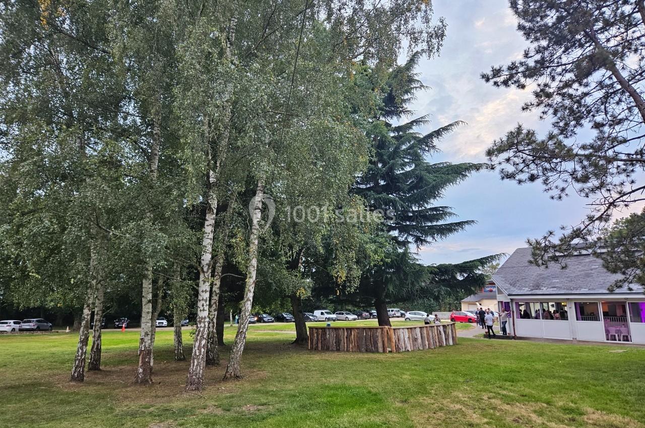 Un groupe d'arbres sur une pelouse près d'un bâtiment blanc avec des voitures garées en arrière-plan.
