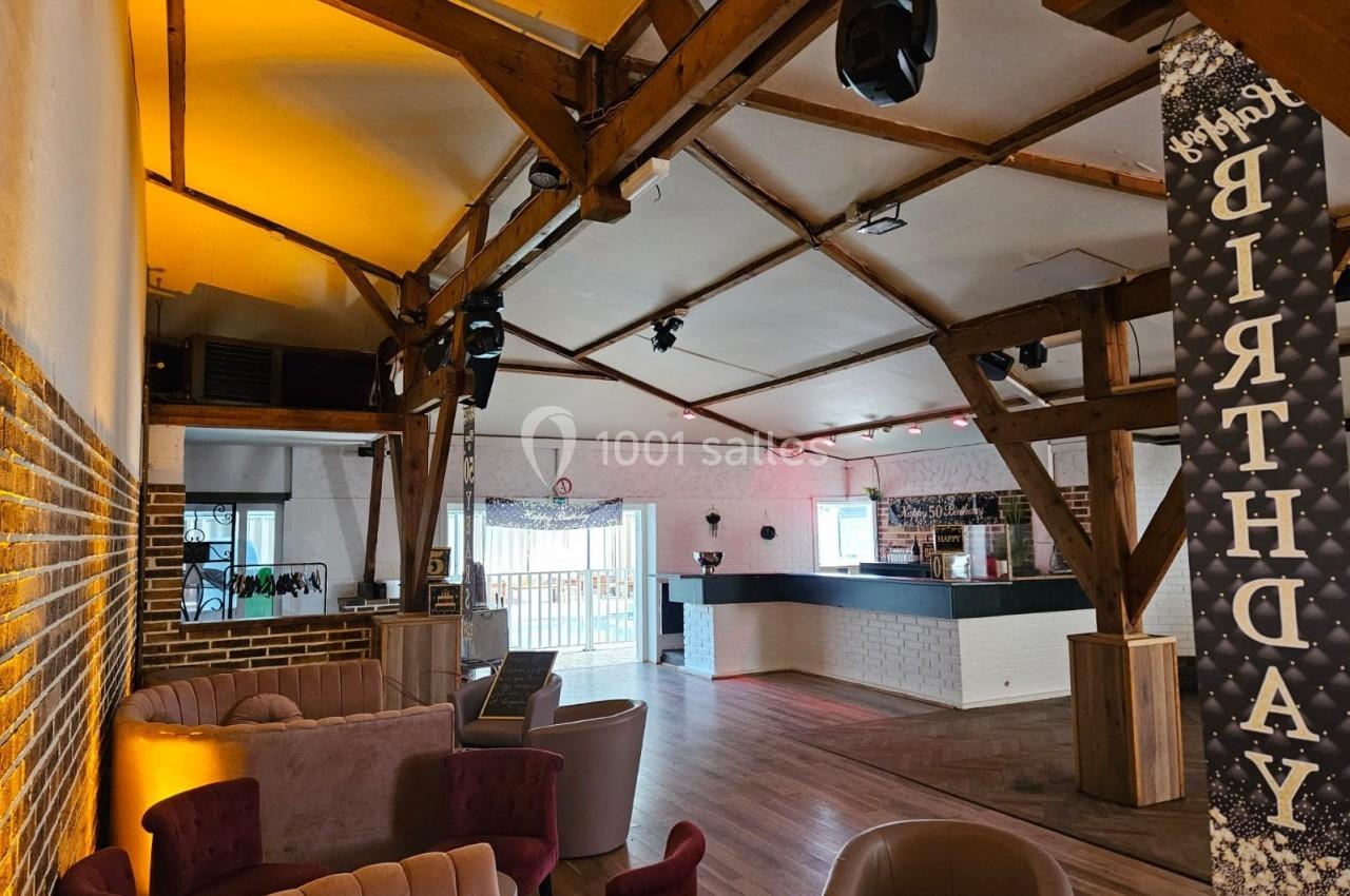 Salle lumineuse avec poutres apparentes, coin salon, comptoir de bar moderne et décoration d'anniversaire.