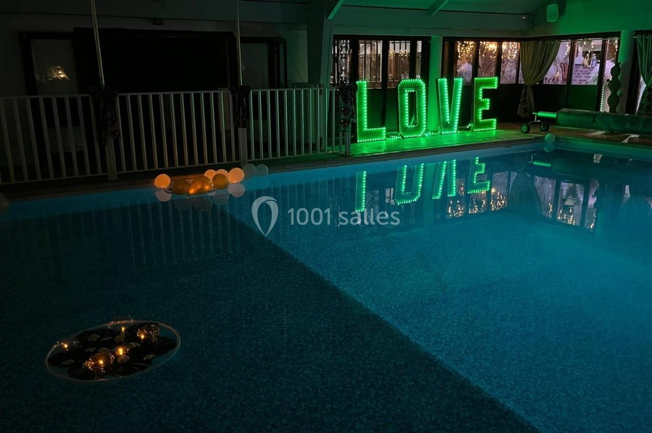 Piscine intérieure éclairée avec des lettres lumineuses vertes formant le mot ’LOVE’ et des bougies flottantes.