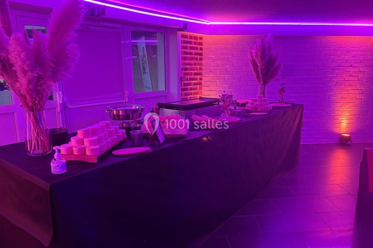 Table de buffet décorée de pampas, éclairée par des lumières violettes, avec plats et condiments disposés.