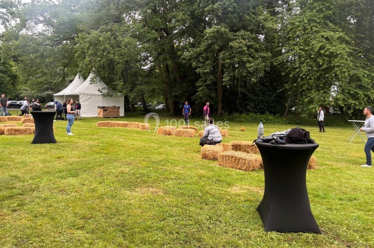 Personnes rassemblées dans un espace extérieur avec des bottes de paille, des tables hautes et des arbres en arrière-plan.