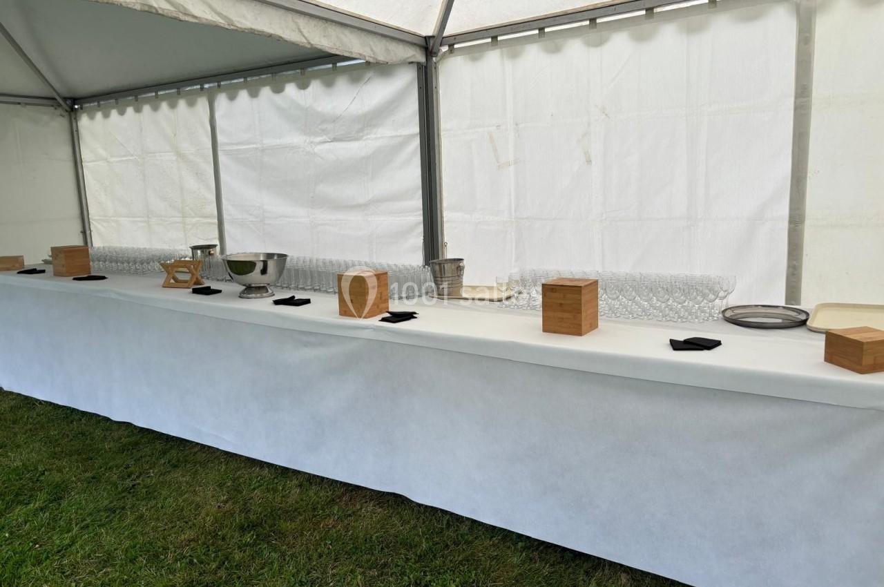Table de buffet sous une tente blanche, avec vaisselle, boîtes en bois et serviettes noires disposées sur une nappe blanche.