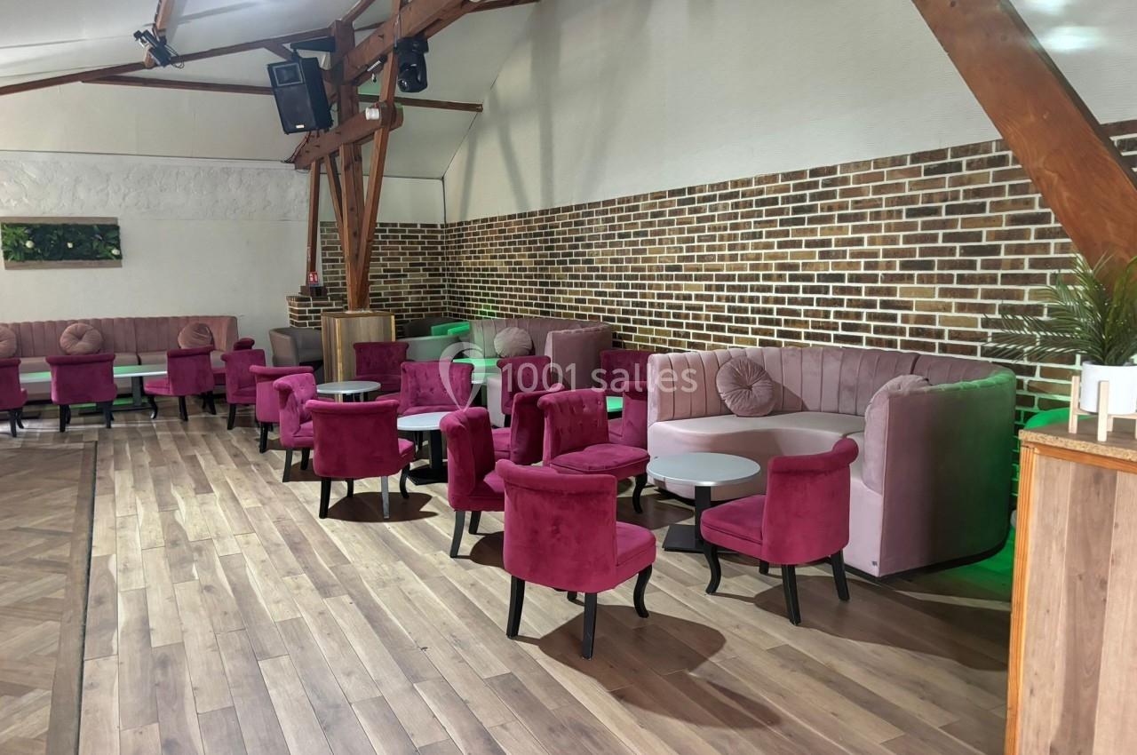 Salle avec des fauteuils roses, tables basses et murs en briques, éclairée par une lumière naturelle.