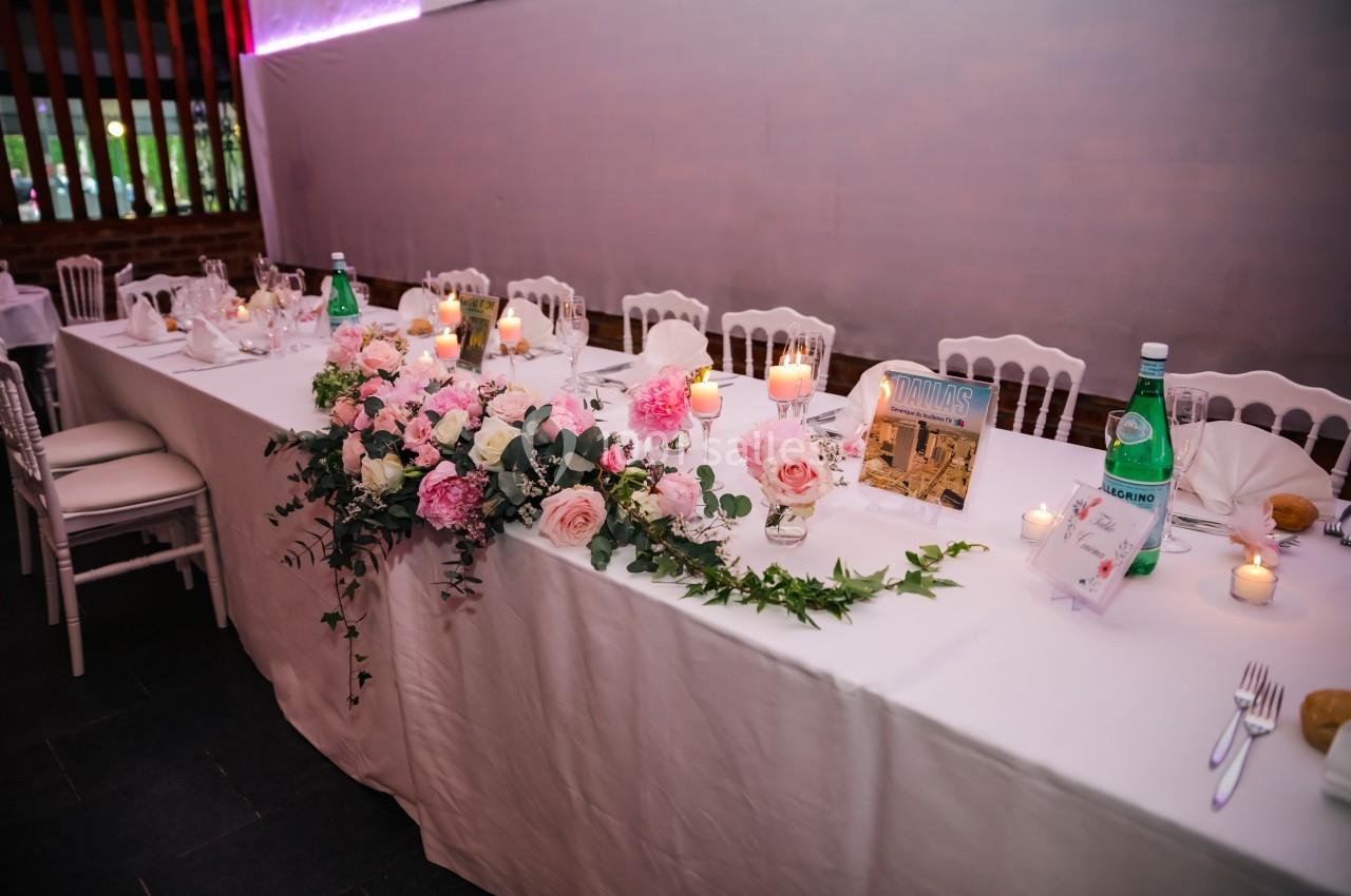 Table de réception décorée de fleurs roses et blanches, bougies allumées et bouteilles d'eau, dans une salle élégante.