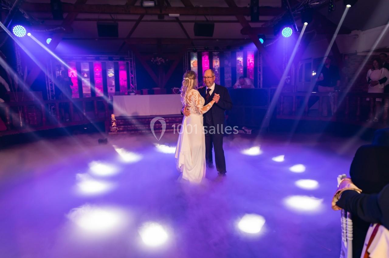 Un couple danse sous des lumières colorées et une ambiance de fumée dans une salle de réception.