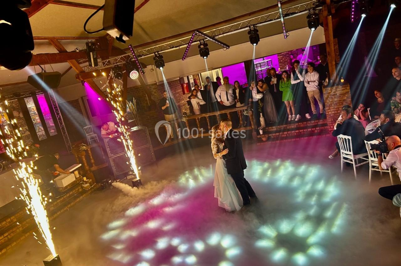 Un couple danse au centre d'une piste entourée de fumée et d'effets pyrotechniques, sous le regard des invités.