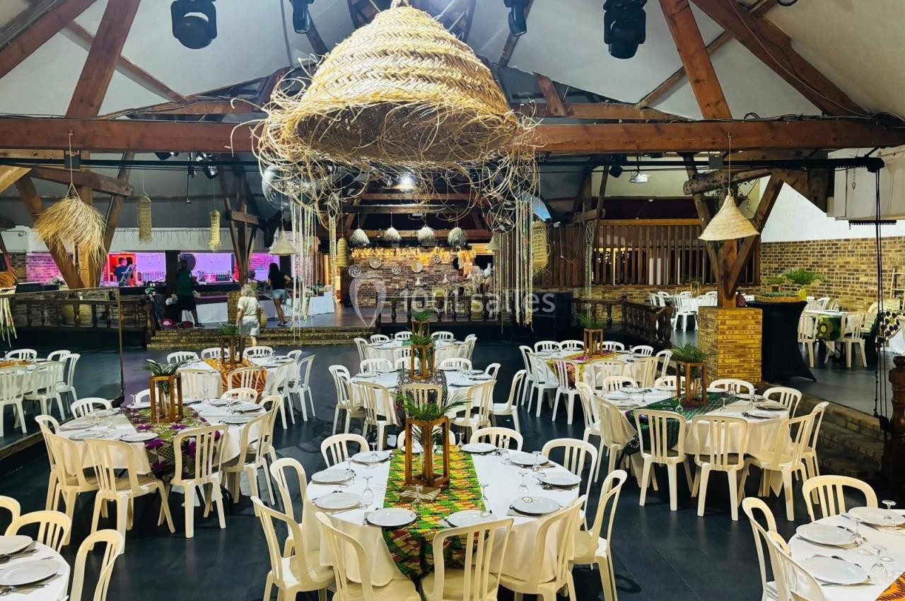 Salle de réception décorée avec des tables rondes dressées, des chaises blanches et des suspensions en osier.