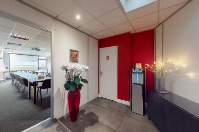 Salle de réunion avec une longue table rectangulaire, chaises noires, projecteur et murs blancs et rouges.