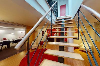 Salle de réunion avec une longue table rectangulaire, chaises noires, projecteur et murs blancs et rouges.