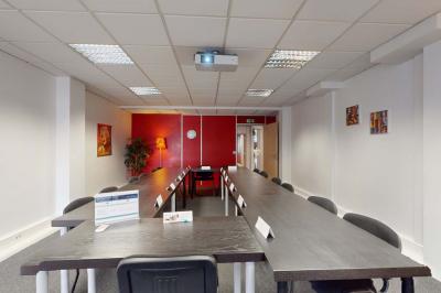 Salle de réunion avec une longue table rectangulaire, chaises noires, projecteur et murs blancs et rouges.