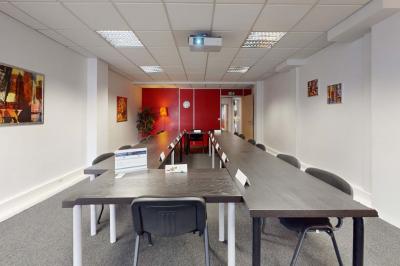 Salle de réunion avec une longue table rectangulaire, chaises noires, projecteur et murs blancs et rouges.