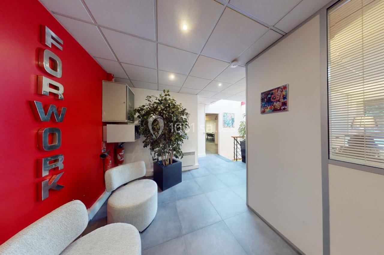 Espace d'accueil avec murs rouges, plantes, sièges arrondis et vue sur un couloir lumineux.