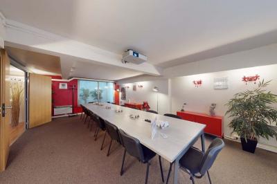 Salle de réunion avec une longue table rectangulaire, chaises noires, projecteur et murs blancs et rouges.