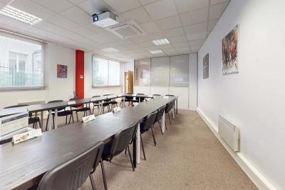 Salle de réunion avec une longue table rectangulaire, chaises noires, projecteur et murs blancs et rouges.