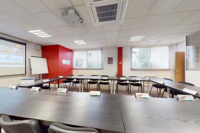 Salle de réunion avec une longue table rectangulaire, chaises noires, projecteur et murs blancs et rouges.