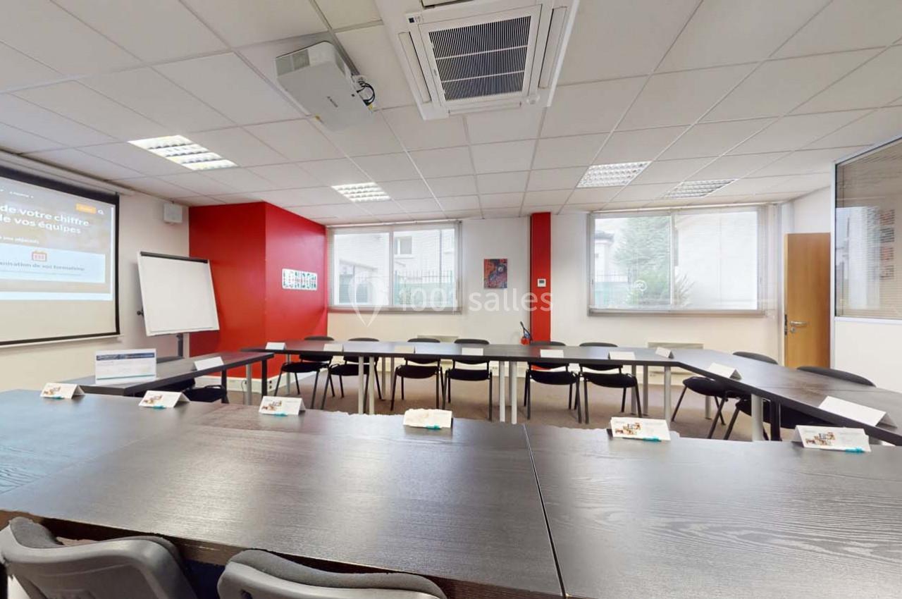 Salle de réunion lumineuse avec tables disposées en U, écran de projection, tableau blanc et fenêtres donnant sur l…