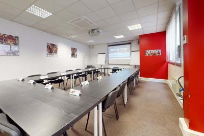 Salle de réunion avec une longue table rectangulaire, chaises noires, projecteur et murs blancs et rouges.