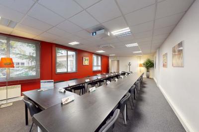 Salle de réunion avec une longue table rectangulaire, chaises noires, projecteur et murs blancs et rouges.